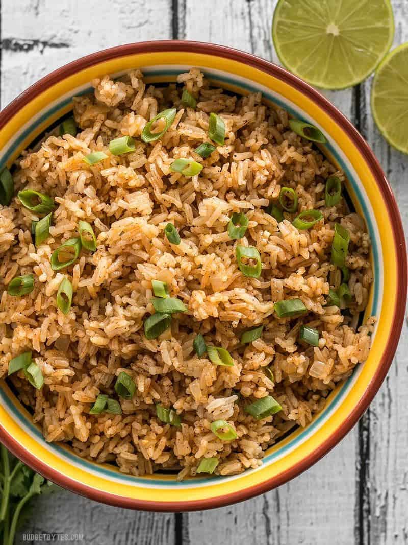 A big bowl of Taco Rice in a striped bowl, garnished with green onions, limes on the side