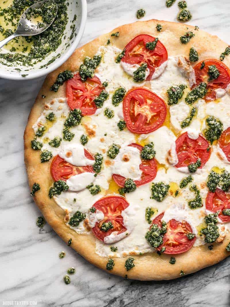 Bowl of parsley pesto next to the white pizza, some pesto drizzled over pizza