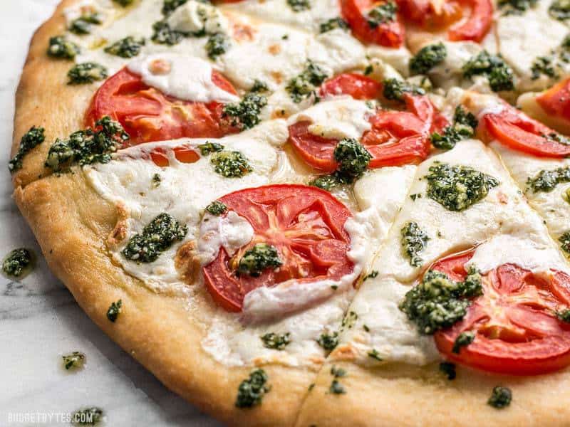 Close side view of White Pizza with Parsley Pesto Drizzle, some spilled on countertop