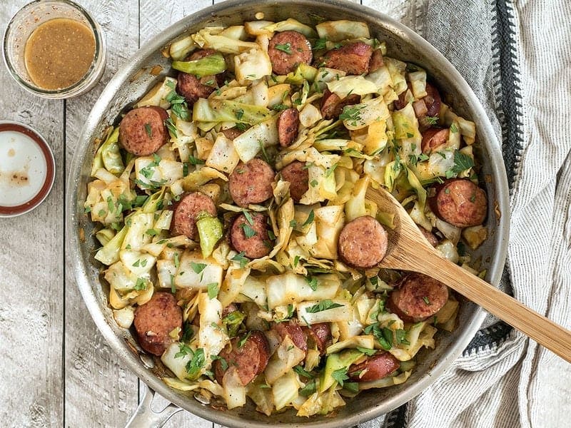 Bird's eye view of Kielbasa and Cabbage Skillet with a jar of tangy mustard vinaigrette. 