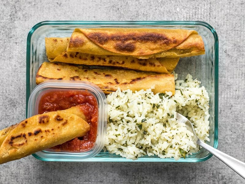 One Creamy Black Bean Taquito being dipped into salsa in the meal prep container