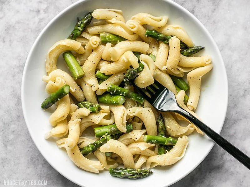 A white bowl full of Lemon Garlic Asparagus Pasta with a black fork