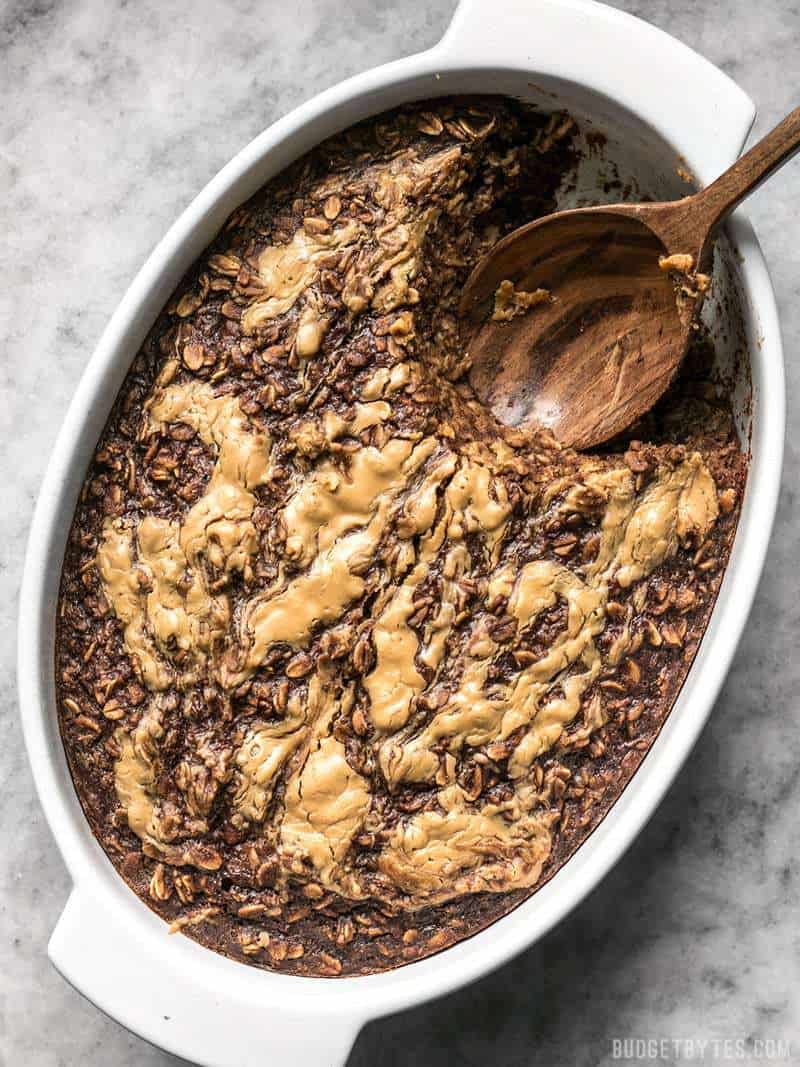 A casserole dish with Peanut Butter Brownie Baked Oatmeal and a wooden spoon scooping a portion