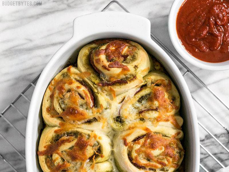 Baked Pesto Pizza Rolls in the baking dish on a cooling rack with pizza sauce on the side