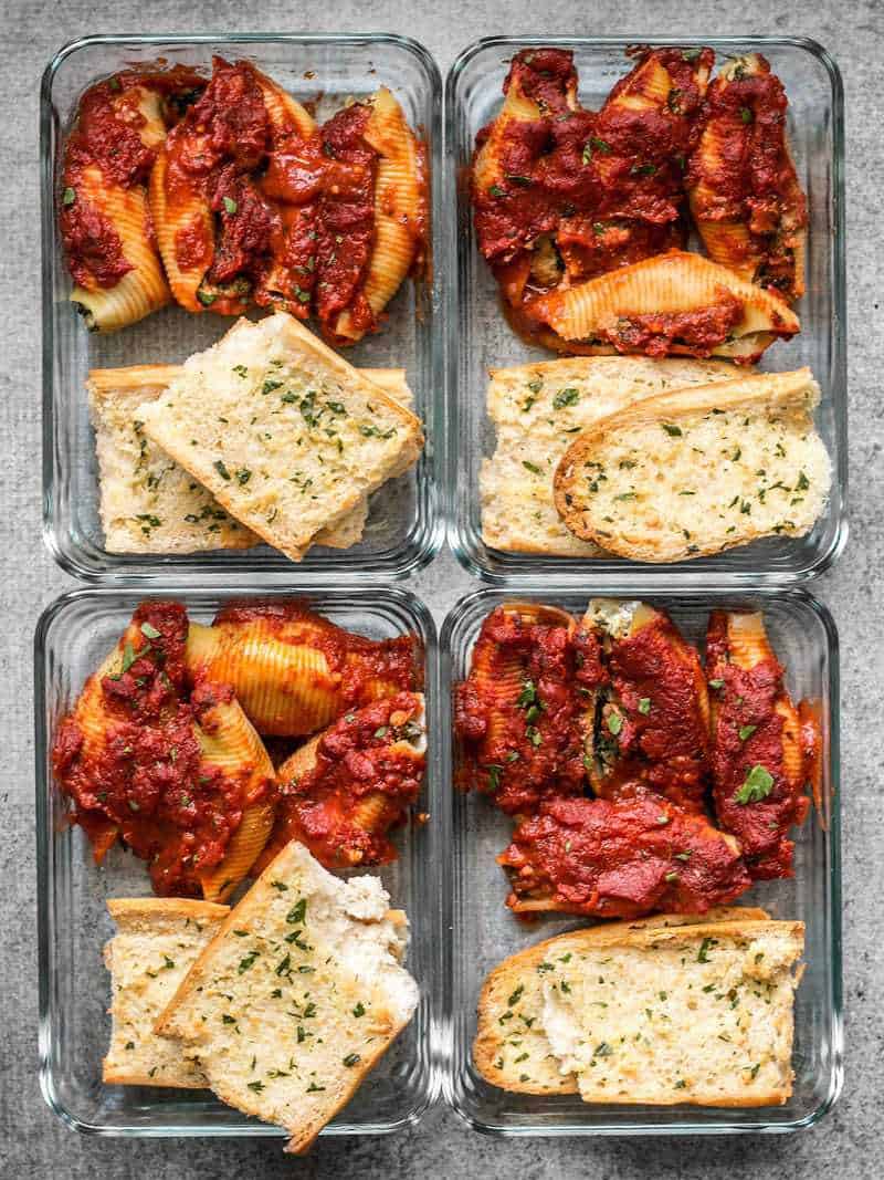 Four glass Pesto Stuffed Shells meal prep containers with homemade garlic bread 