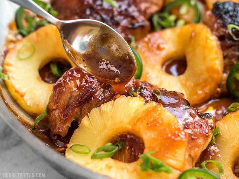 Close up of BBQ sauce being drizzled over chicken thighs with slices of pineapple.