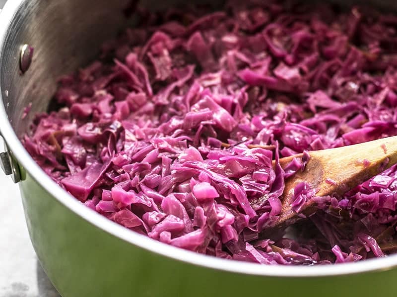 Side view of Braised Red Cabbage in a large pot with a wooden spoon.