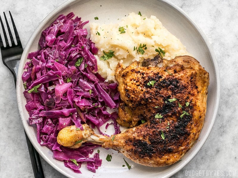 Braised Red Cabbage on a plate with a roasted chicken leg and mashed potatoes.