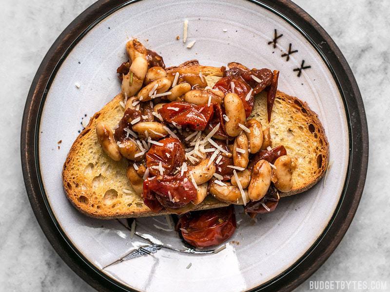 Overhead shot of a piece of Garlic Toast with Blistered Tomatoes and White Beans, topped with shredded Parmesan