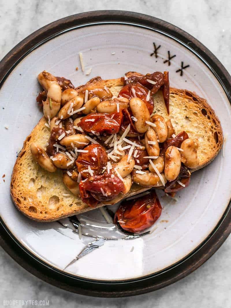 A piece of Garlic Toast with Balsamic Tomatoes and White Beans on a single plate with a wooden charger
