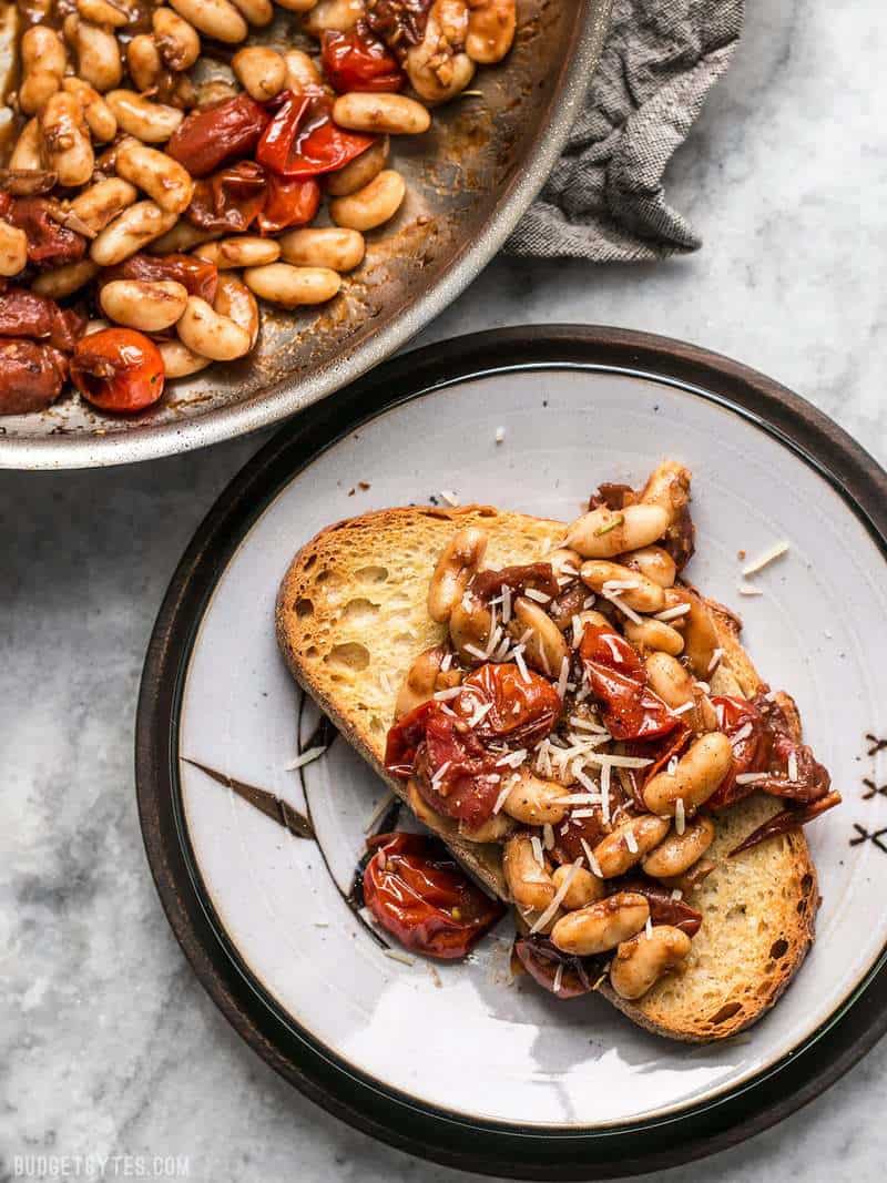 A piece of Garlic Toast with Balsamic Tomatoes and White Beans on a plate next to the skillet