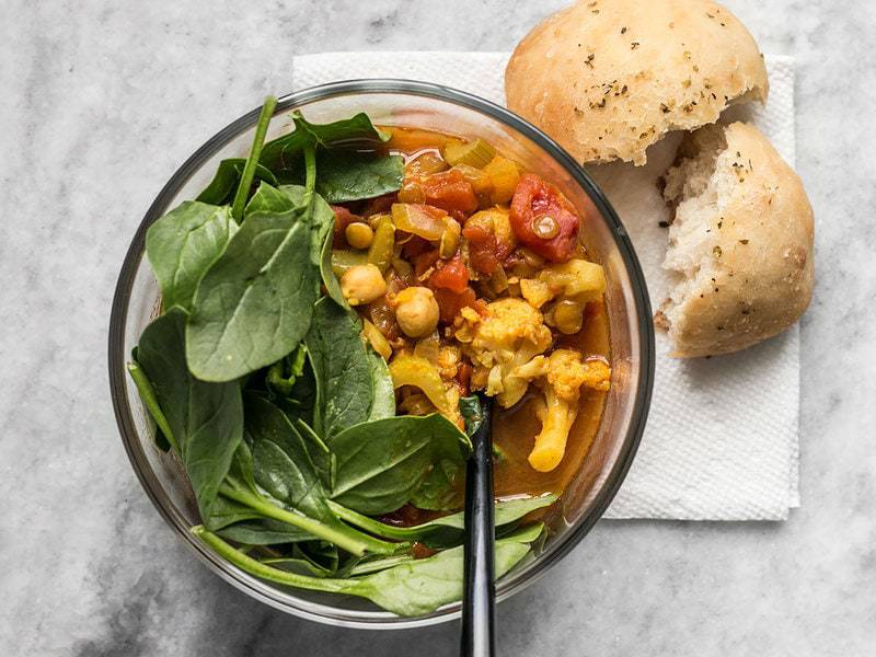 One bowl of Moroccan Lentil and Vegetable Stew with spinach and a focaccia roll