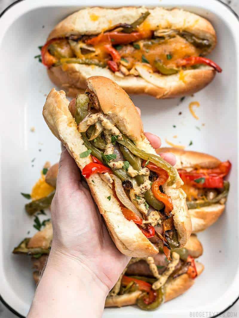Close up of a Roasted Bratwurst with Peppers and Onions, in a bun with mustard.