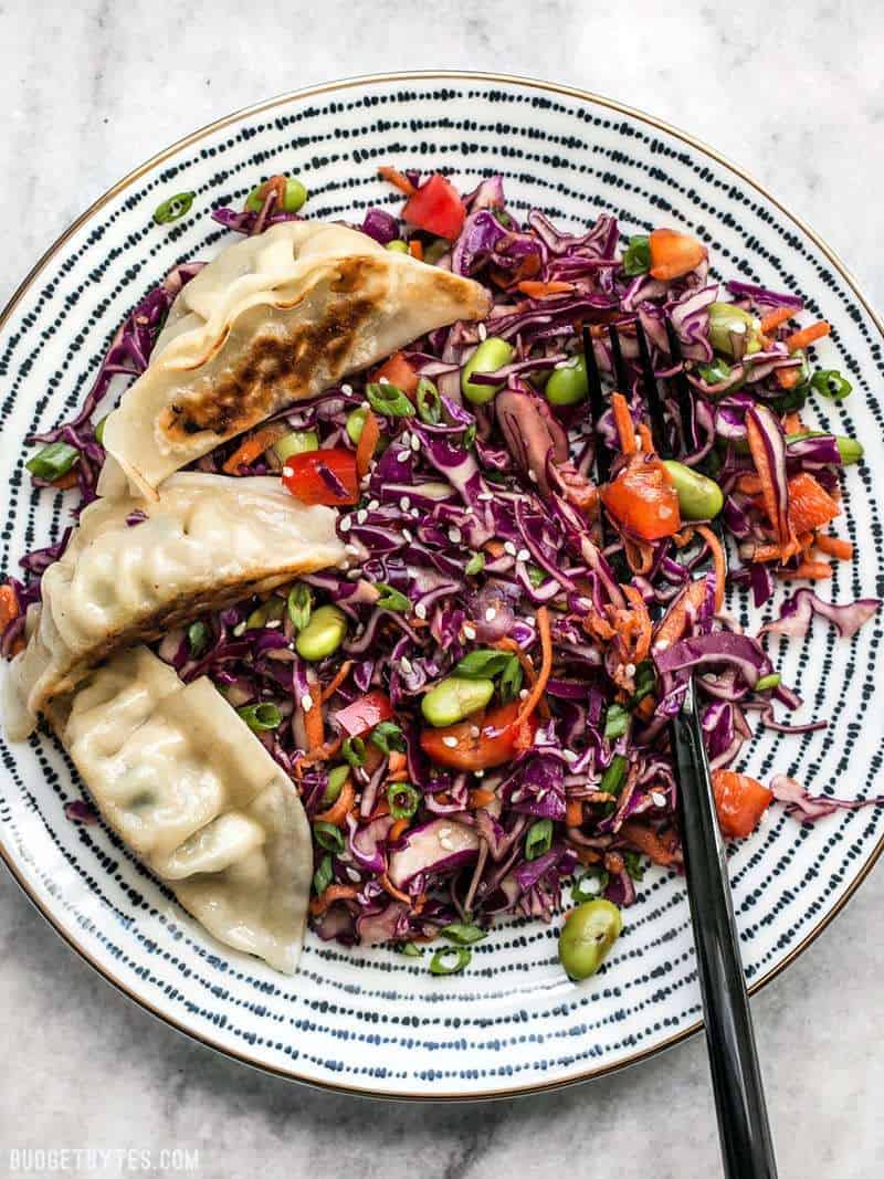 A plate full of Sesame Slaw with Edamame, topped with three gyoza. 