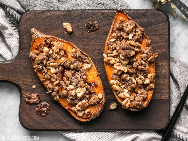 Overhead shot of two Streuseled Sweet Potatoes on a wooden cutting board