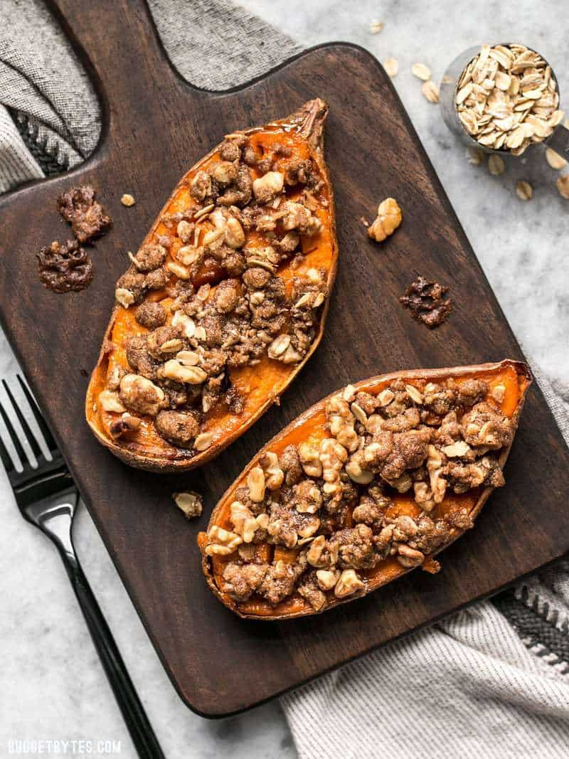 Two Streuseled Sweet Potatoes on a wooden cutting board with a fork.