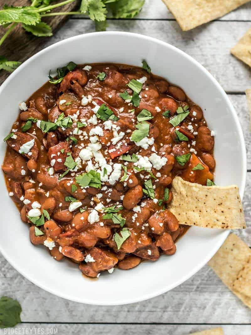 A bowl full of Instant Pot Pinto Beans with Chorizo, with tortilla chips and cheese and cilantro on top.