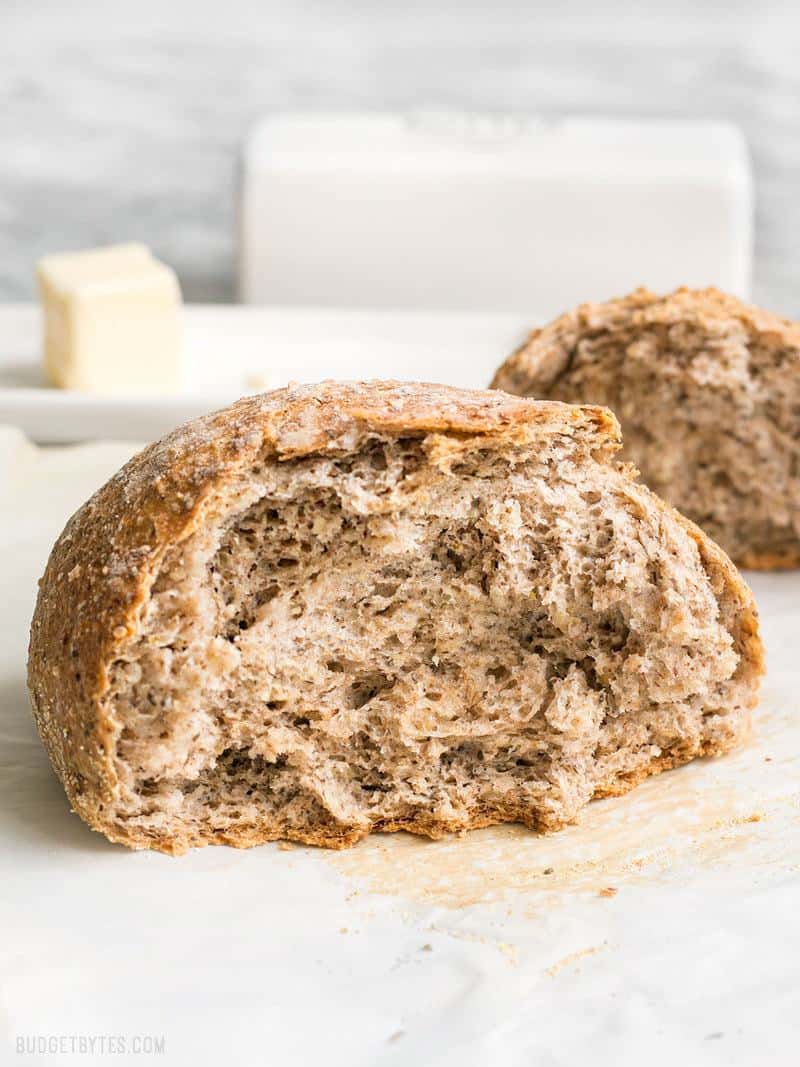 A loaf of Seeded No-Knead Bread torn in half facing camera, butter in the background