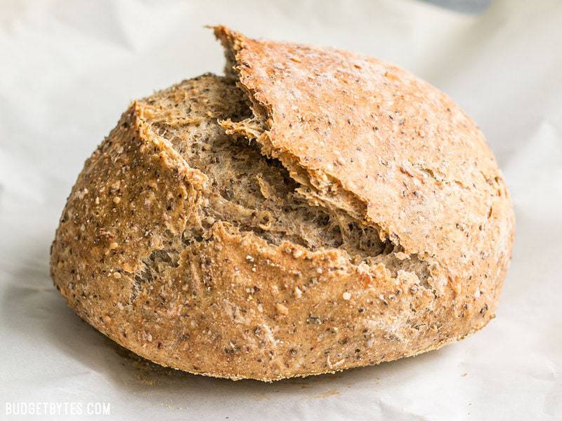 A whole loaf of freshly baked Seeded No-Knead Bread on parchment