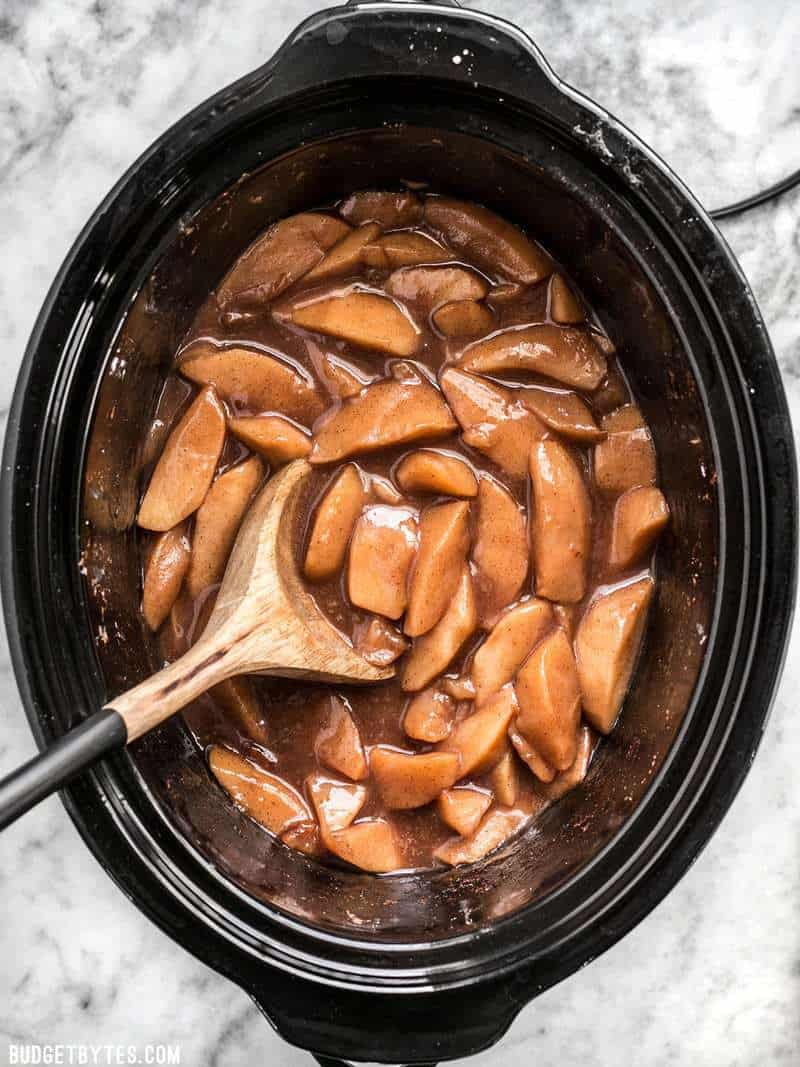 Finished Slow Cooker Hot Buttered Apples in a slow cooker with a wooden spoon.
