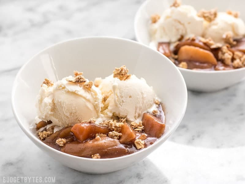 Two bowls of Slow Cooker Hot Buttered Apples topped with ice cream and granola
