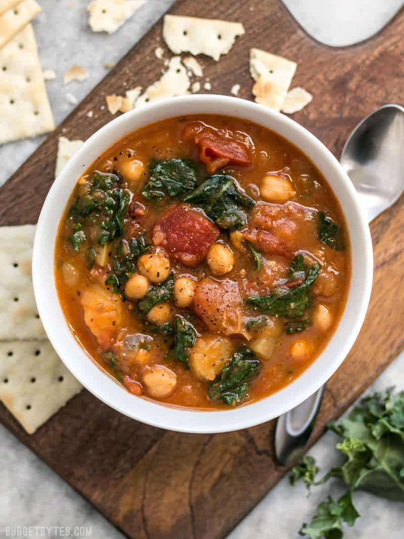 A bowl of Smoky Potato Chickpea Stew on a wooden cutting board surrounded by saltine crackers. 