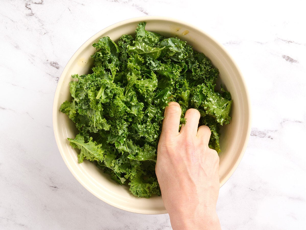 A hand massaging kale in a bowl.
