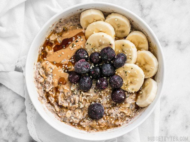 A bowl of prepared Make Ahead Seeded Oats with bananas, blueberries, and peanut butter