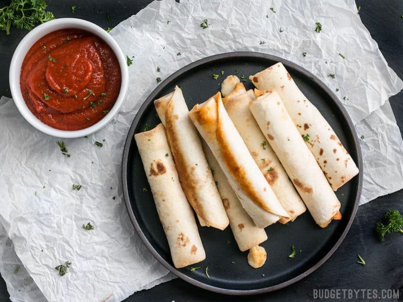 A plate full of Pizza Roll Ups with a bowl of pizza sauce on the side