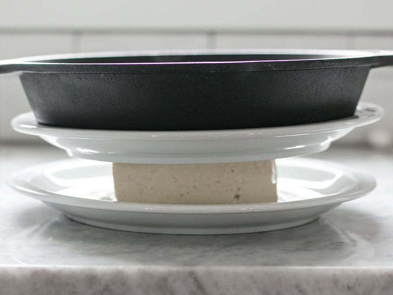 Press Tofu using plates and a heavy object like a cast iron skillet