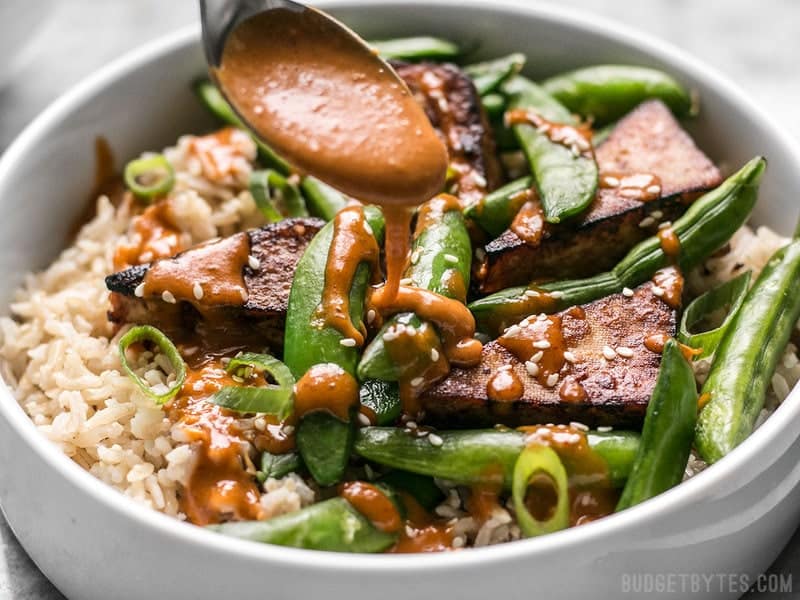 Spicy Peanut Sauce being drizzled on a Soy Marinated Tofu Bowl