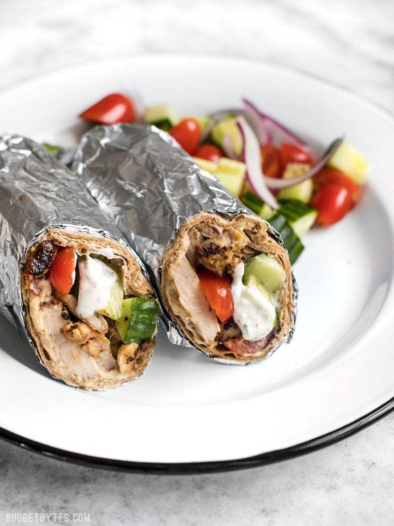 Greek Chicken Wraps wrapped in foil on a plate with salad