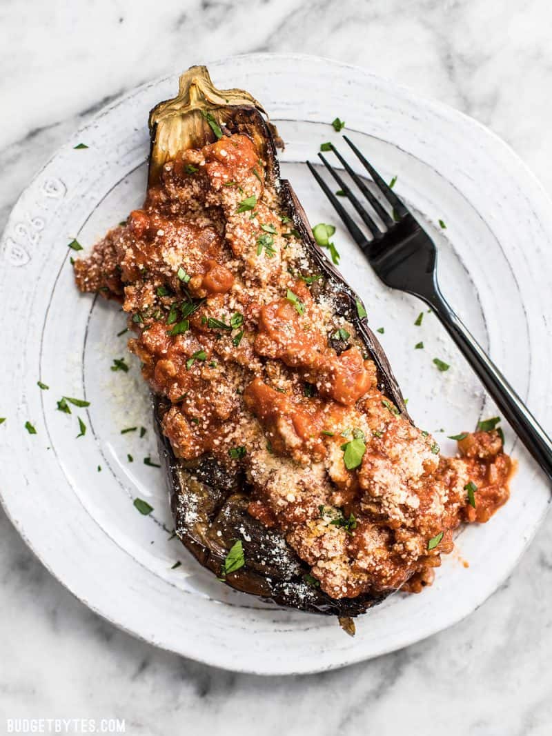 One Roasted Eggplant with Meat Sauce on a white plate with black fork, sprinkled with Parmesan and parsley