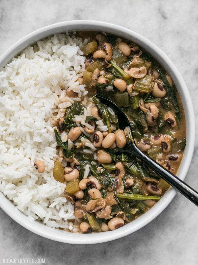 A large bowl of Slow Simmered Black Eyed Peas with Greens, served with rice.