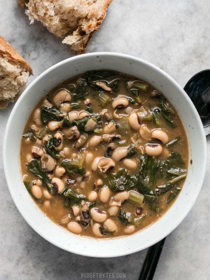 A bowl full of Slow Simmered Black Eyed Peas with greens, served with crusty bread.