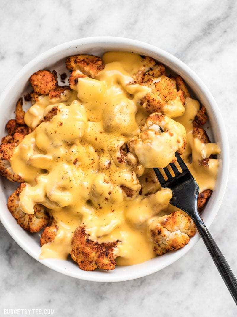 A big bowl of Spicy Roasted Cauliflower with Cheese Sauce being eaten with a black fork