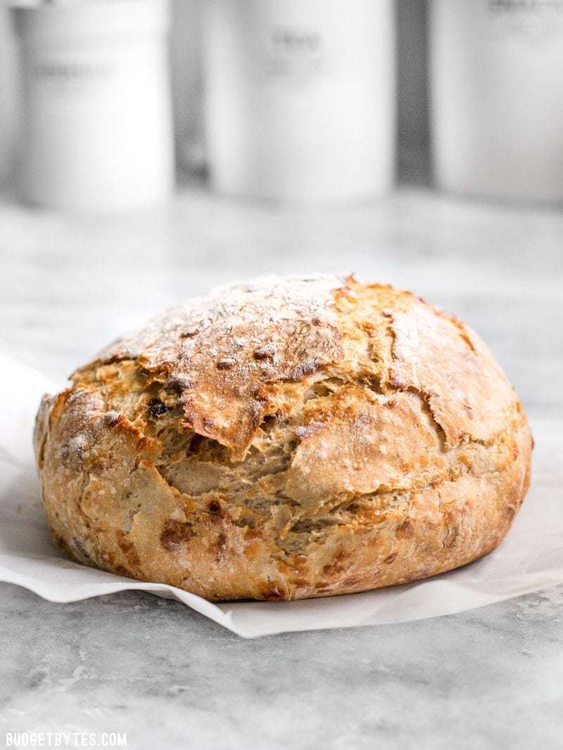 Side view of a freshly baked loaf of Tomato Basil No Knead Bread on parchment