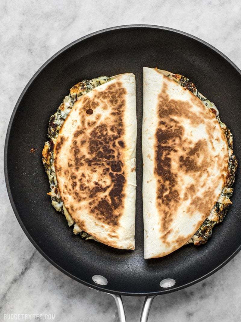 Two Spinach Artichoke Quesadillas being toasted in a skillet
