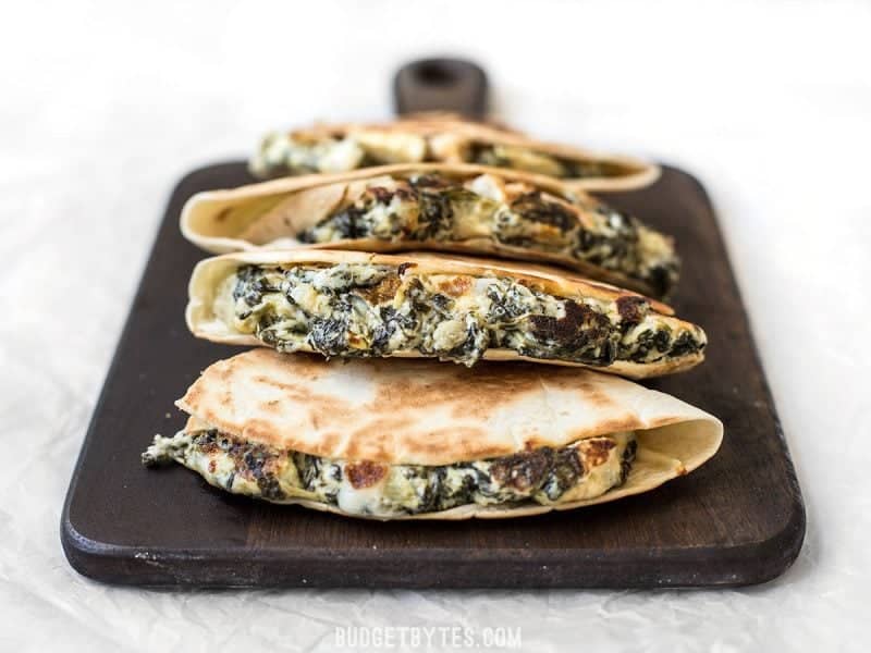 Front view of overstuffed Spinach Artichoke Quesadillas stacked on a cutting board