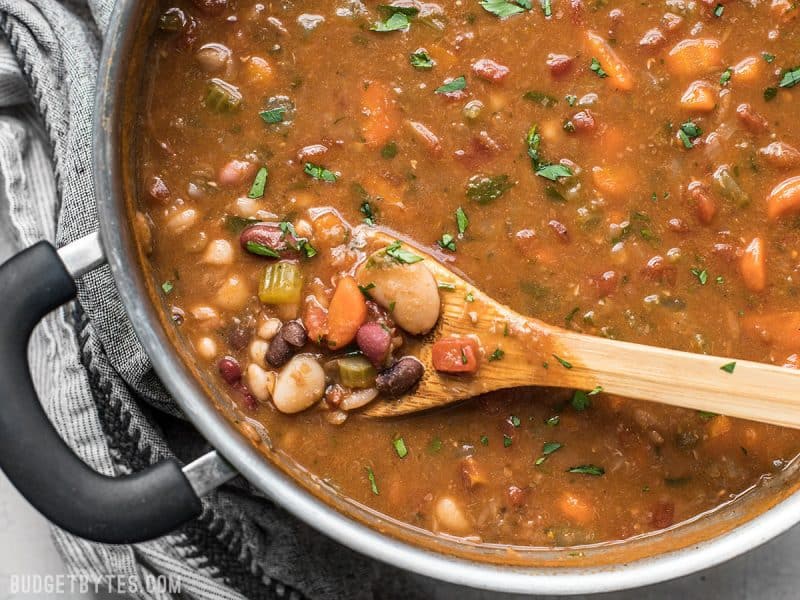 A close up view of a pot of Vegetarian 15 Bean Soup with a wooden spoon.