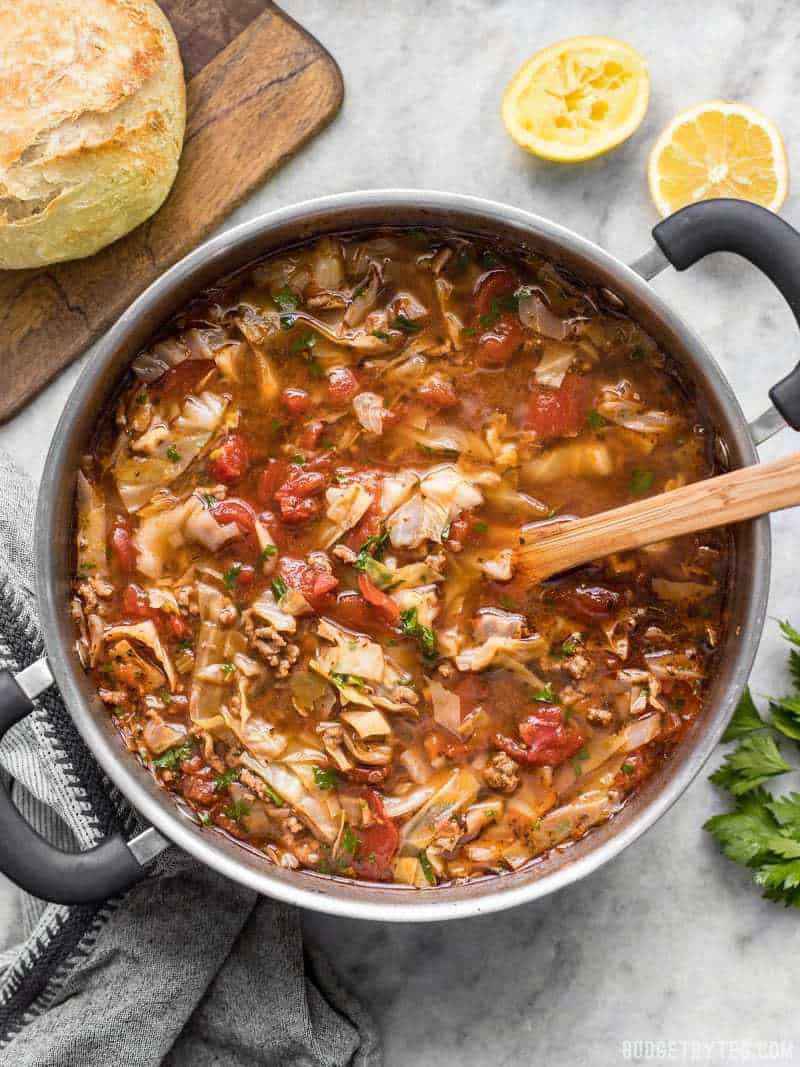 A full pot of finished Beef and Cabbage Soup with bread on the side and a wooden spoon