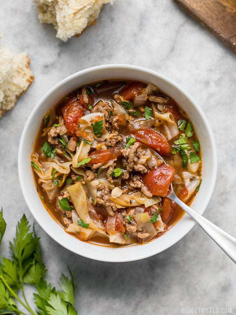 A bowl of Beef and Cabbage Soup with chunks of crusty bread near by