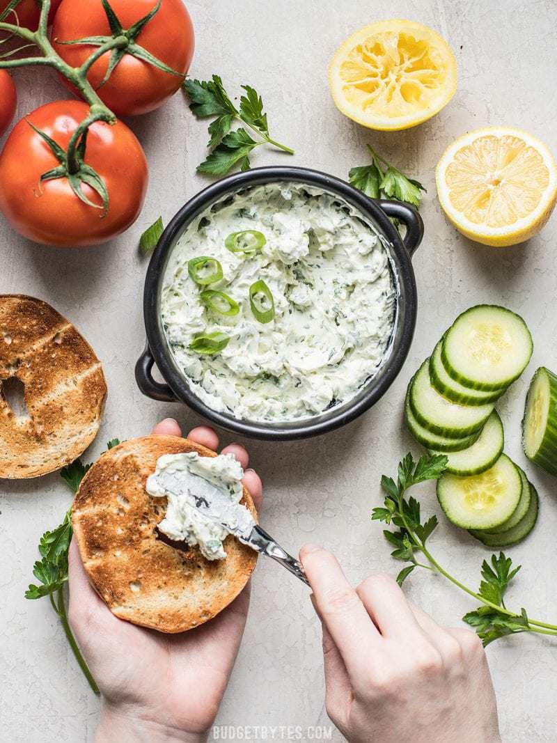 Scallion Herb Cream Cheese Spread being smeared onto a toasted bagel