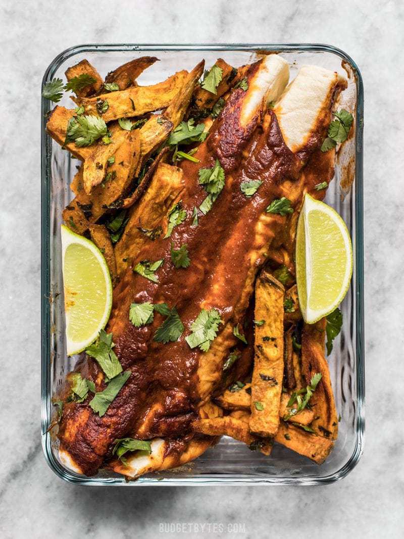 Black Bean and Avocado Enchiladas in a glass meal prep container with Cilantro Lime Sweet Potato Sticks