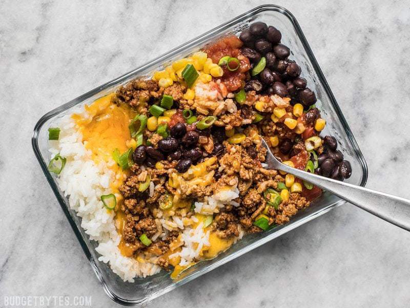 One rectangular glass meal prep container filled with a burrito bowl. A fork mixing the contents.