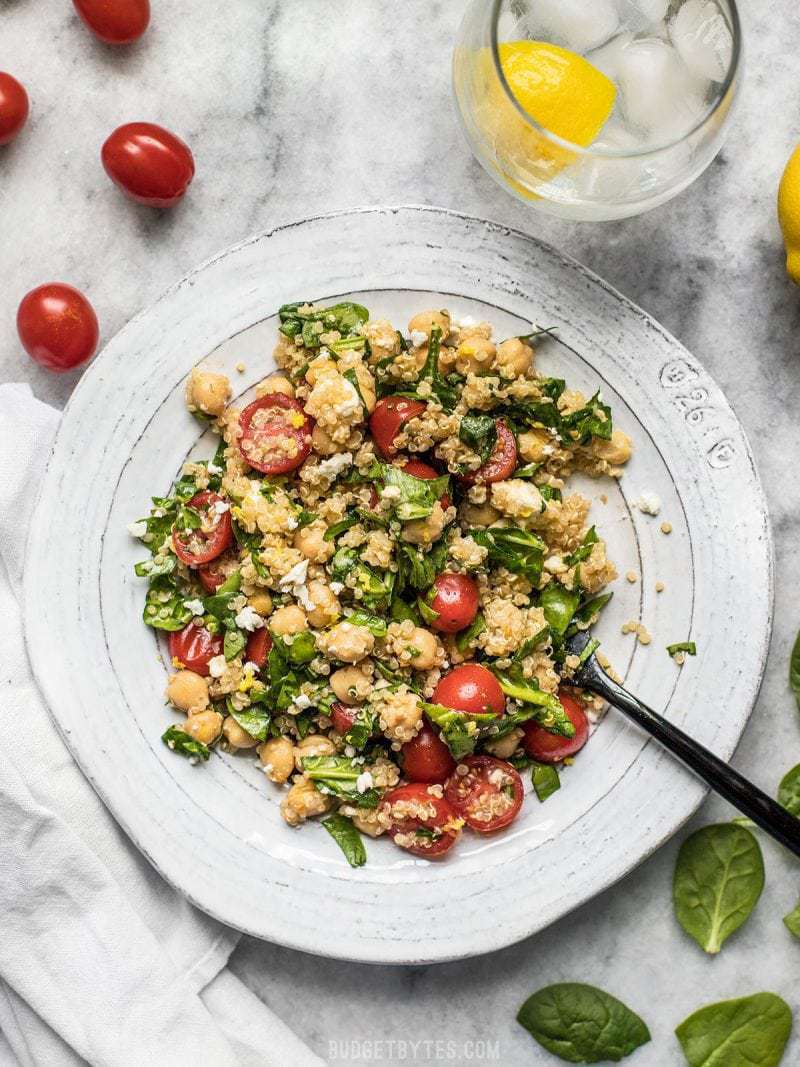 A plate full of Spinach Chickpea and Quinoa Salad with a glass of lemon water, tomatoes, and spinach on the side