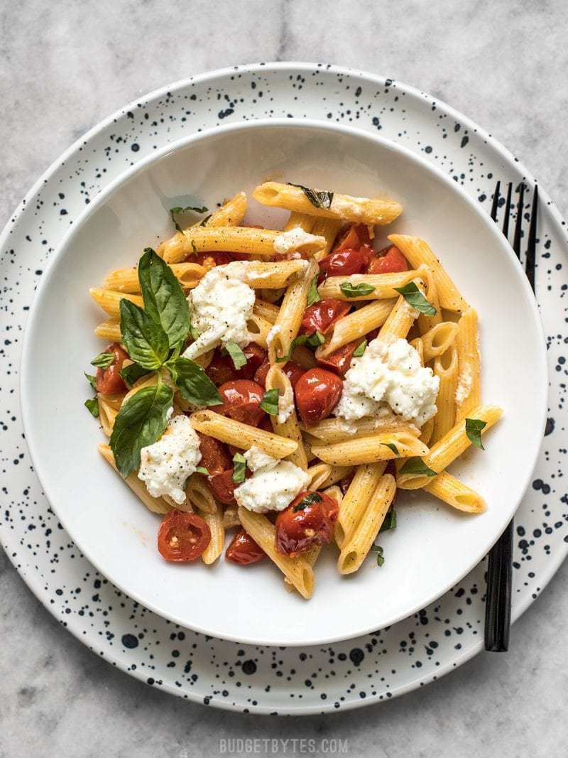 A shallow bowl full of Fresh Tomato Basil Pasta with Ricotta on a speckled plate. 