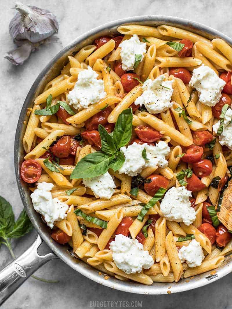 A skillet full of Fresh Tomato Basil Pasta with Ricotta. Fresh basil on top, garlic on the side. 