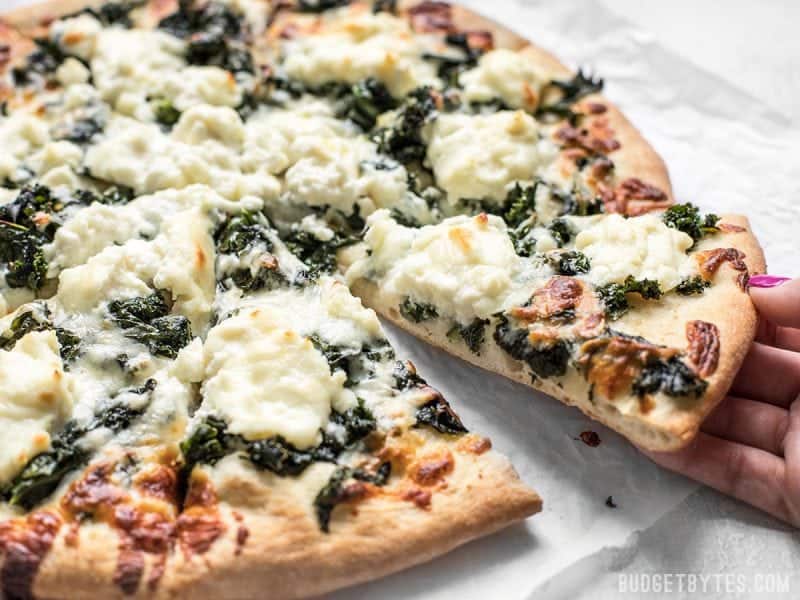 A hand picking up a piece of Garlicky Kale and Ricotta Pizza