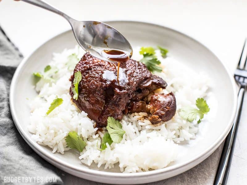 Honey Hoisin Garlic Sauce being drizzled over a piece of chicken on a bed of rice.